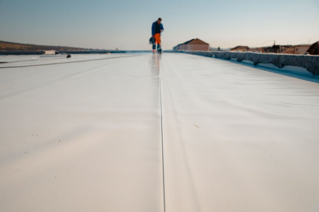Man on a commercial building doing roofing work | TPO roof seam welding