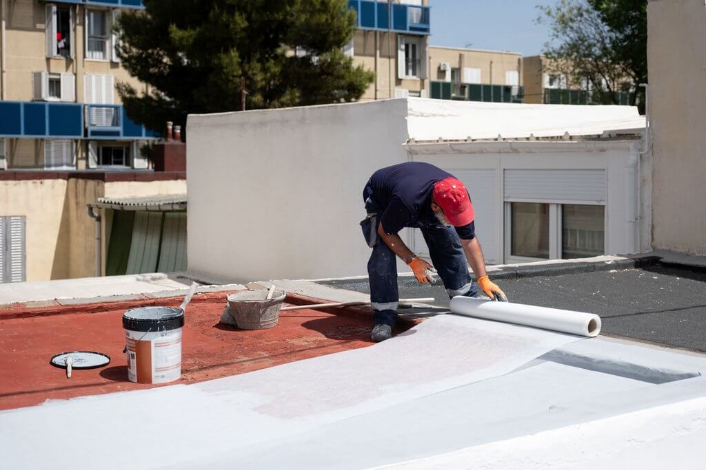 Man on a roof working on a commercial roofing project laying down waterproof material